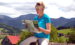 Radlerin studiert ihre Radkarte in einer herrlichen Berglandschaft mit grünen Hügeln und vereinzelten Häusern