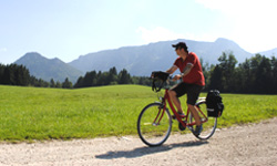 Einzelner Radler vor grüner Wiese, im Hintergrund eine beeindruckende Bergkulisse