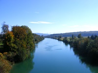 Blick auf die sich zwischen grünen Ufern dahinschlängelnde Aare, ganz im Hintergrund einige schneebedeckte Alpengipfel